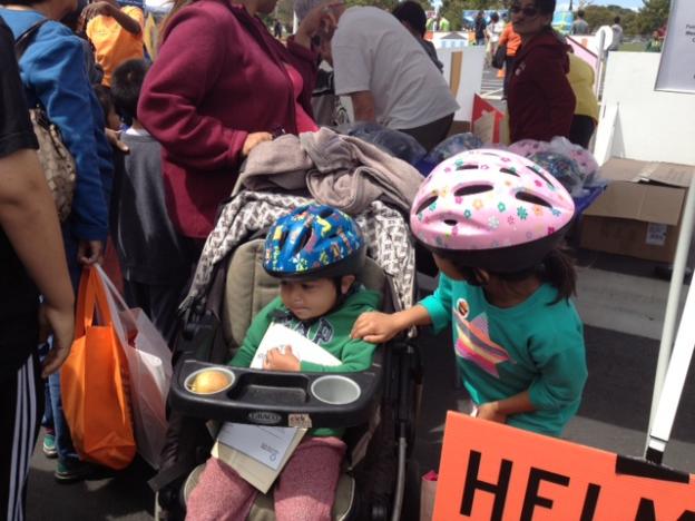 A young cyclist in a pretty new helmet checks her little brother’s fit.